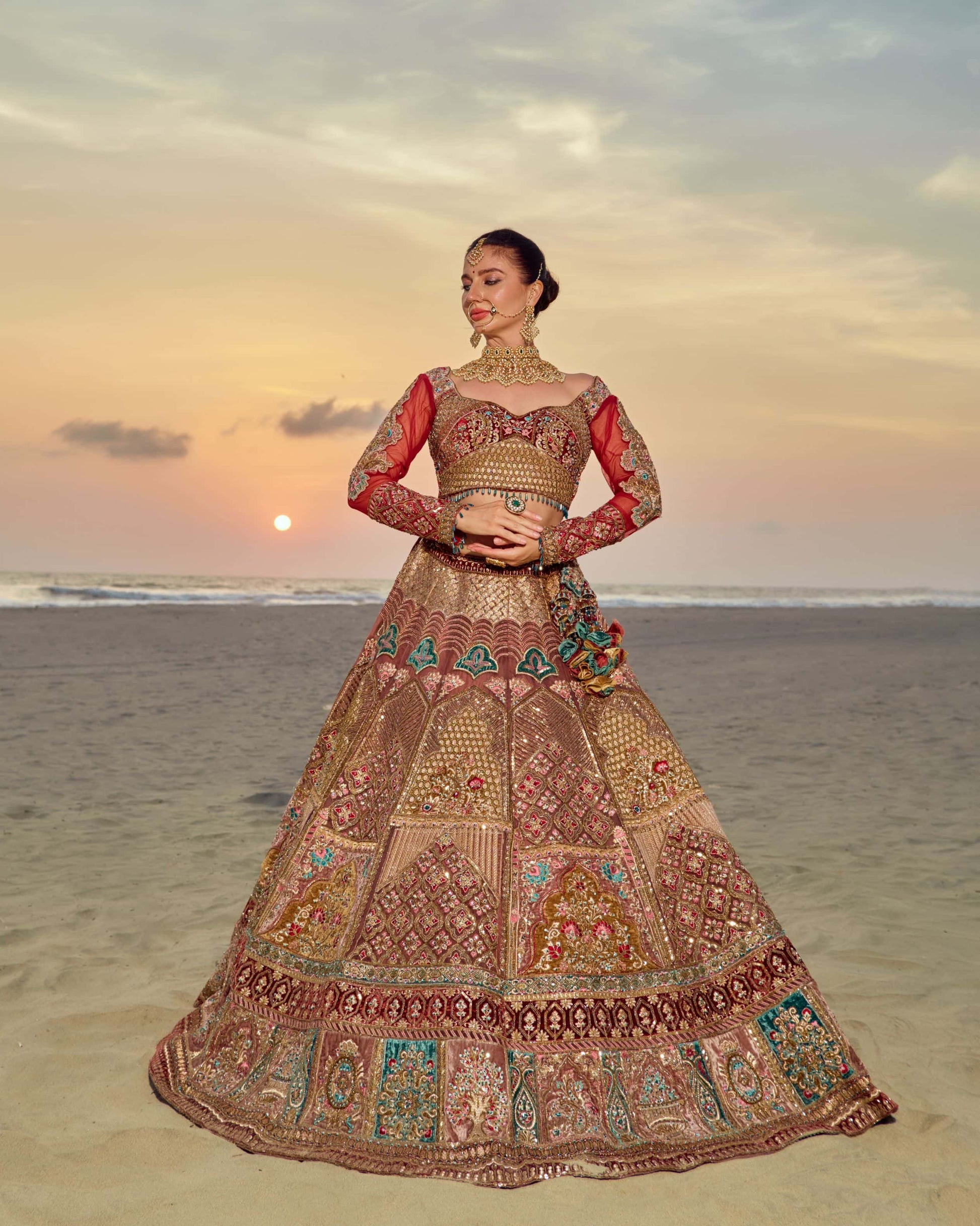 Woman in a traditional embroidered outfit standing on a beach at sunset.