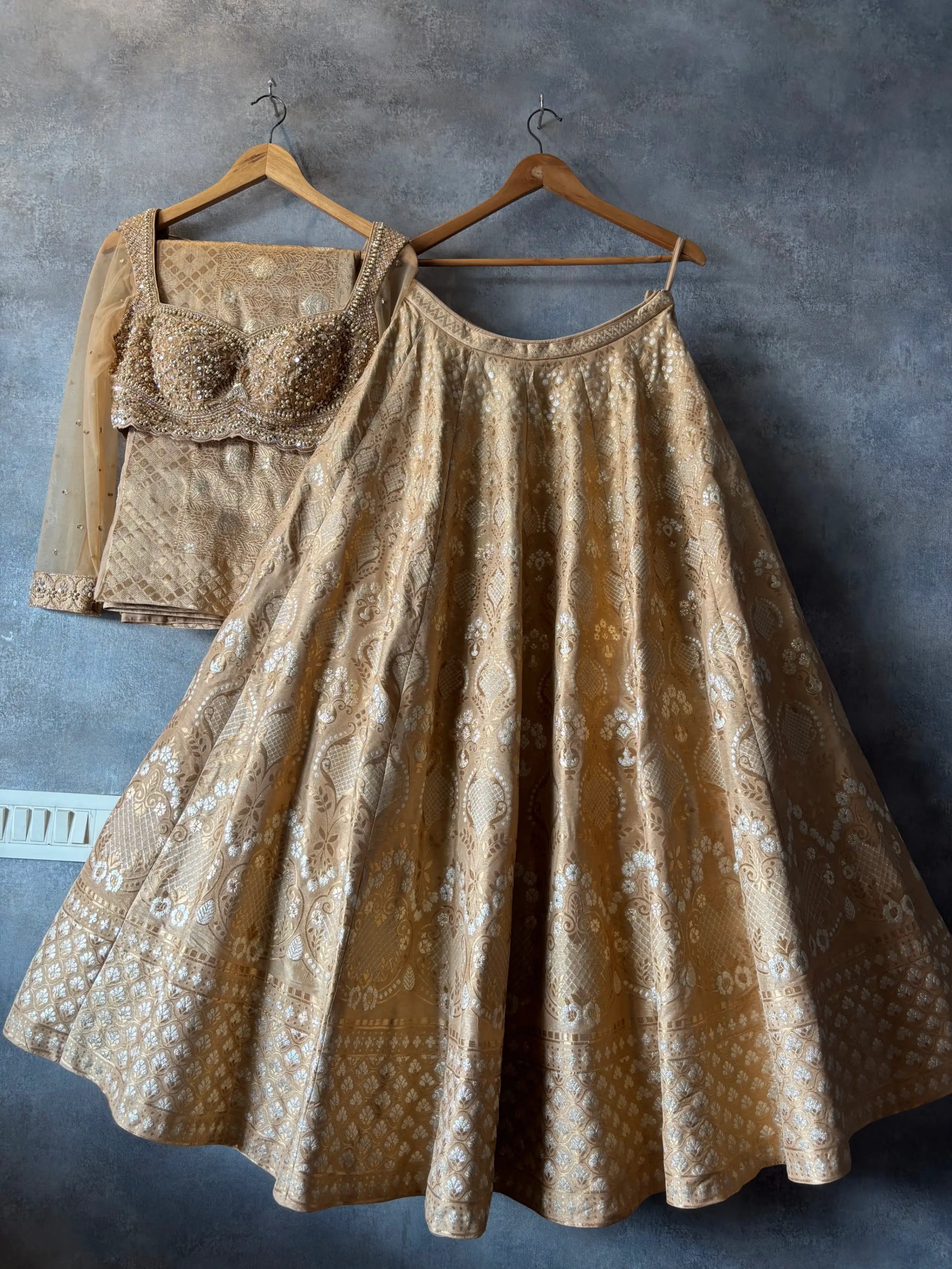 Gold patterned dress and bra on hangers against a gray wall