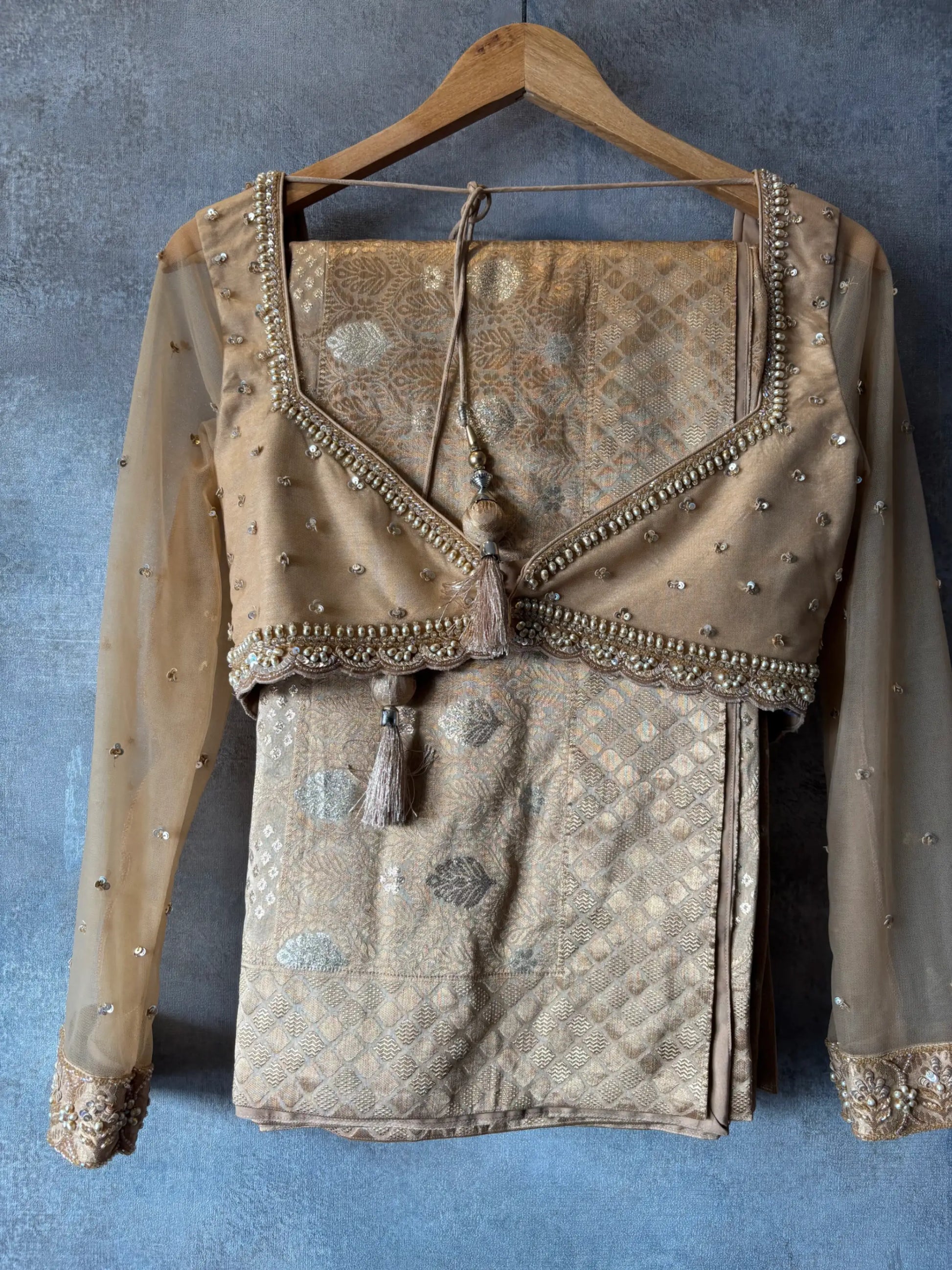 Decorative blouse with intricate patterns and embellishments on a hanger against a gray background