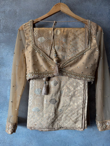 Decorative blouse with intricate patterns and embellishments on a hanger against a gray background