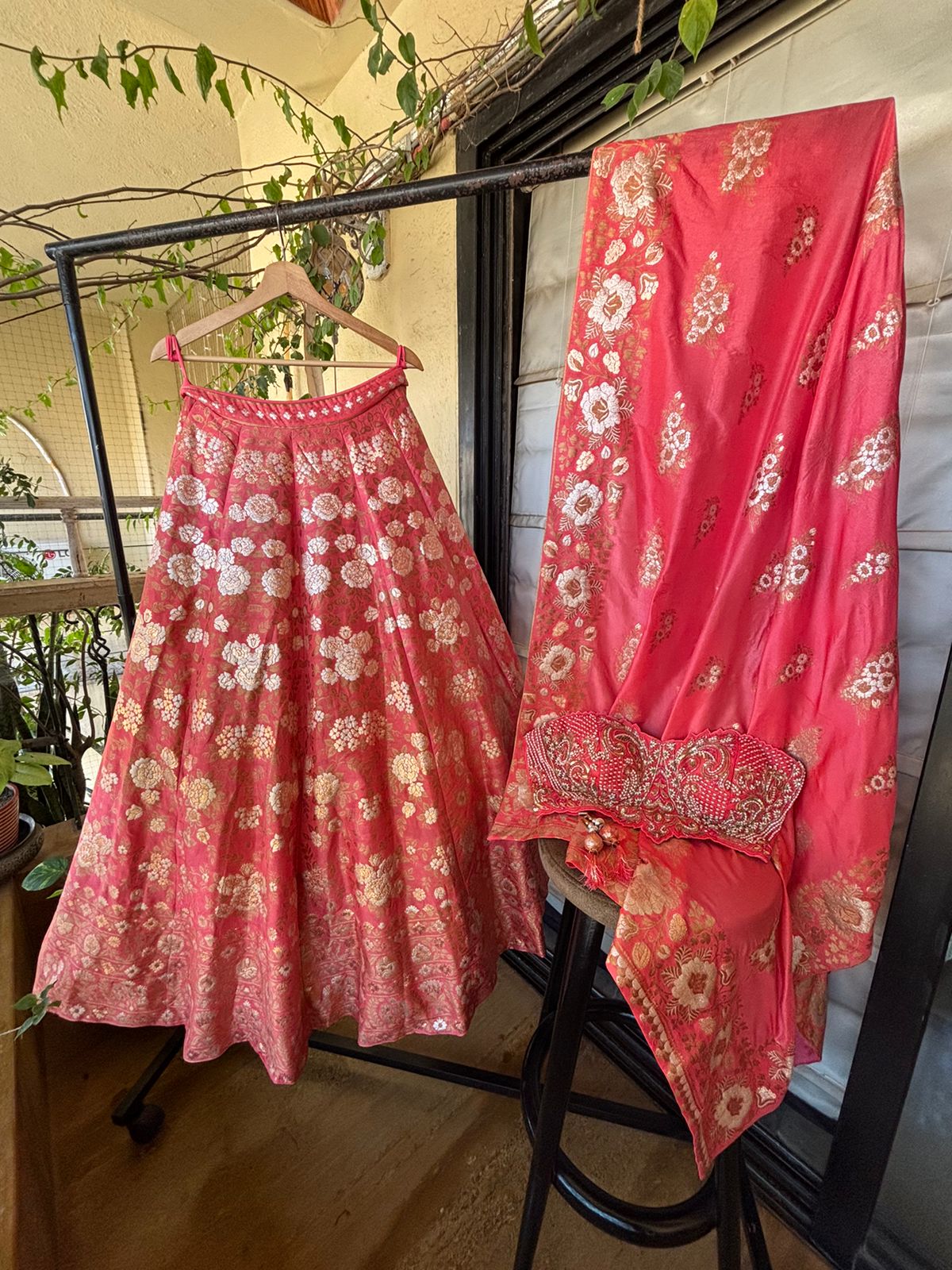 Red floral traditional outfit with a dupatta on a stand outdoors.