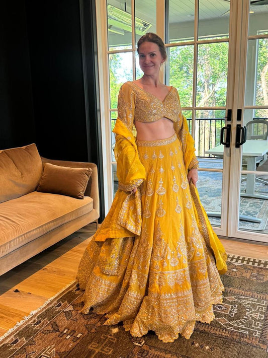 Woman in a yellow and gold traditional outfit standing in a room with a couch and large window.