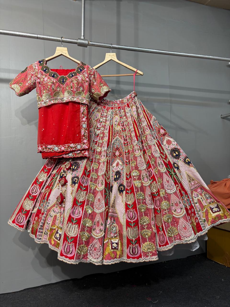 Traditional outfit with a floral blouse and red lehenga on hangers against a gray wall.