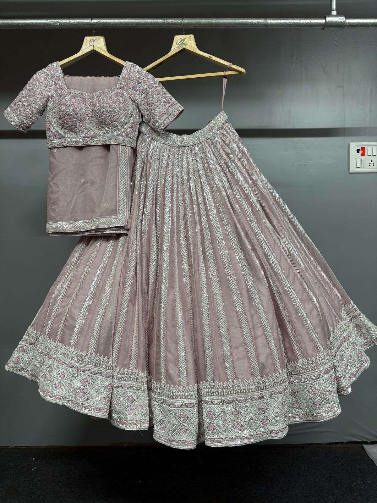 Gray embroidered lehenga with blouse on a hanger against a dark background