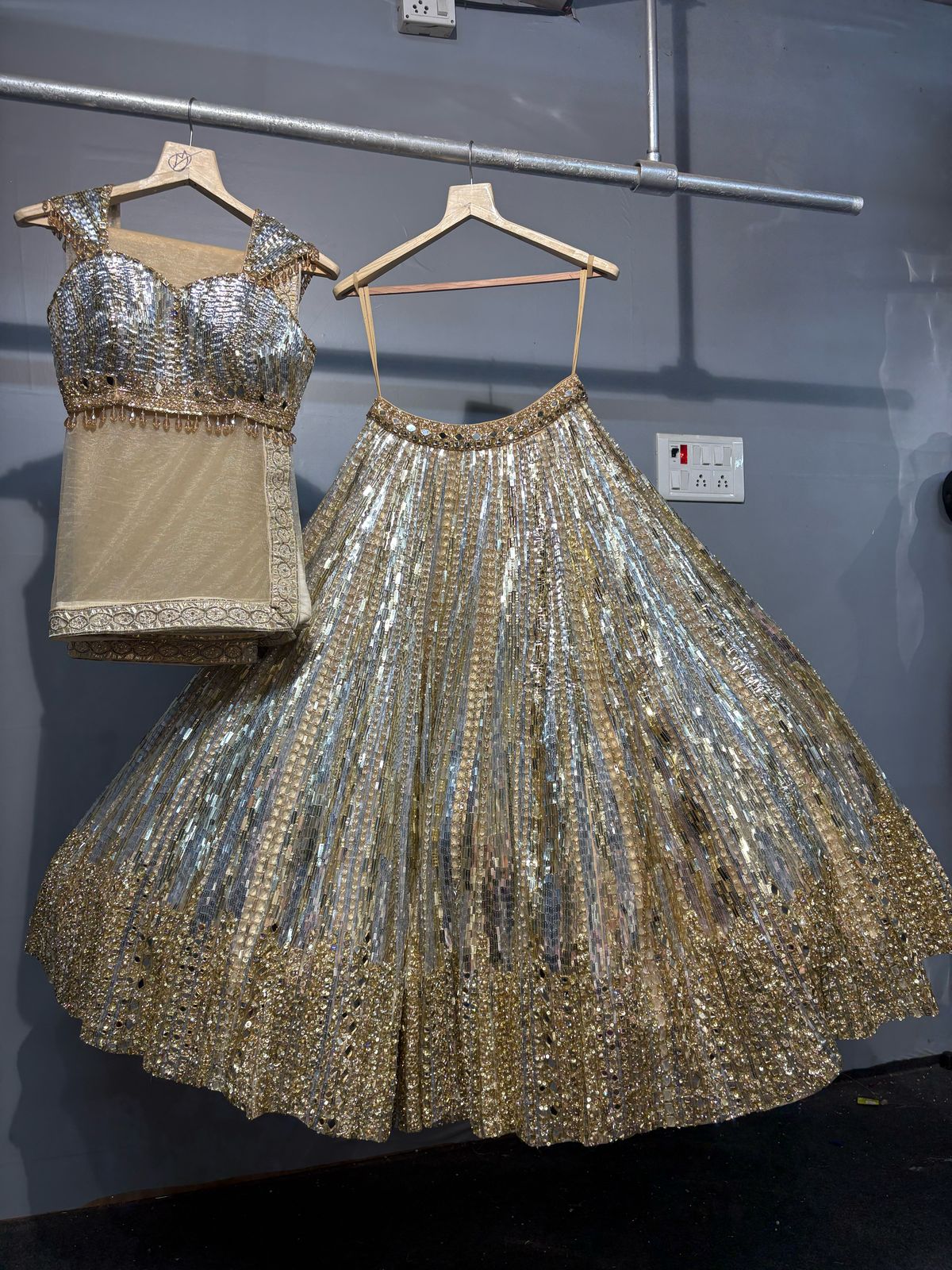 Silver sequin top and skirt set on hangers against a gray wall.