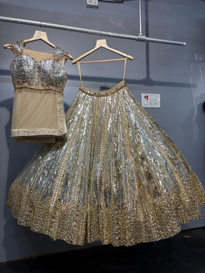 Silver sequin top and skirt set on hangers against a gray wall.