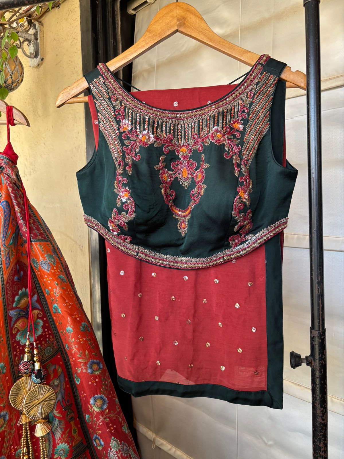 Traditional embroidered blouse on a hanger with a colorful dupatta in the background.