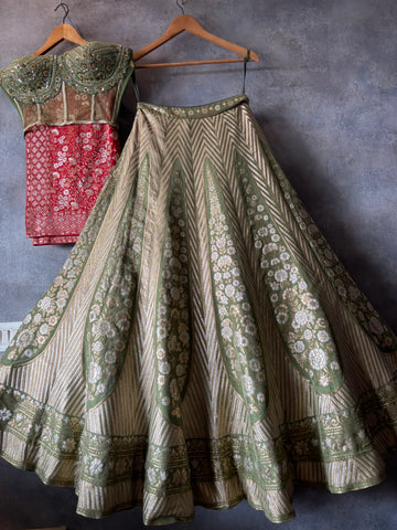 Traditional outfit with a red blouse and green and white patterned skirt on hangers against a gray wall.