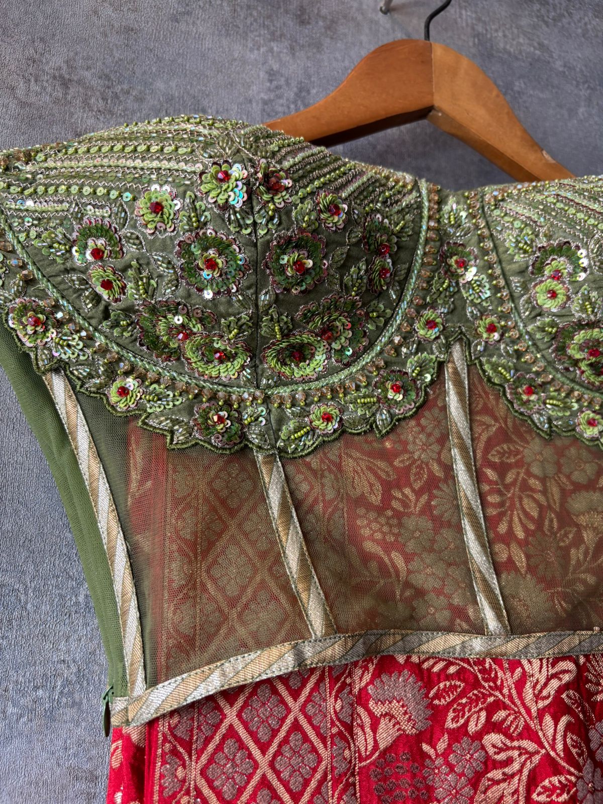 Decorative blouse with intricate green embroidery on a hanger against a gray background